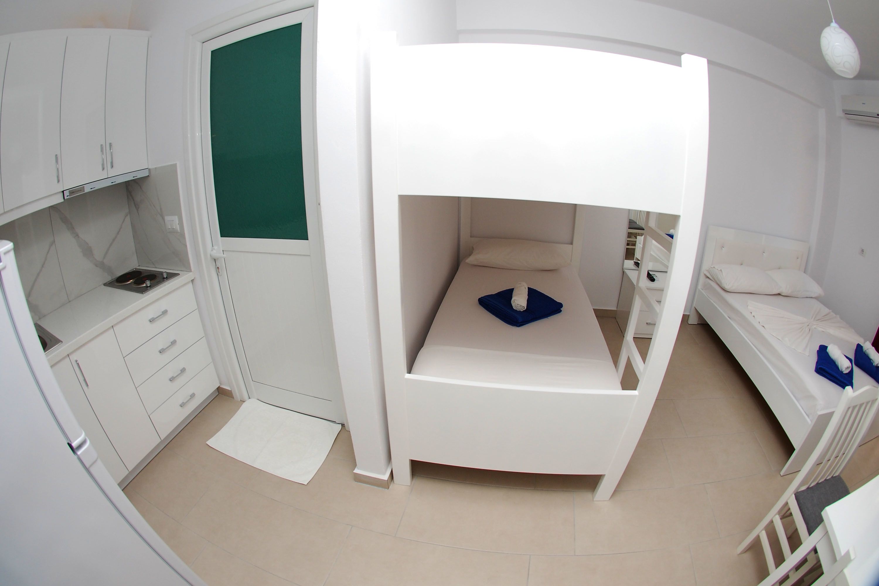 A compact room with a bunk bed, a small kitchenette, and a single bed.