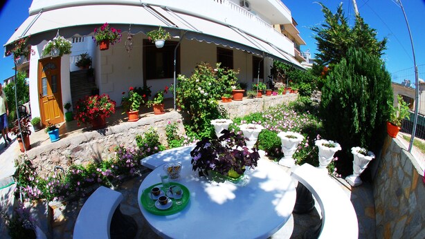 Un patio con una mesa redonda, plantas en macetas y un edificio de fachada blanca y techo curvo.