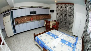 Una habitación compacta con cama, una mesita y una silla. Cuenta con una kitchenette equipada con refrigerador, estufa y microondas.