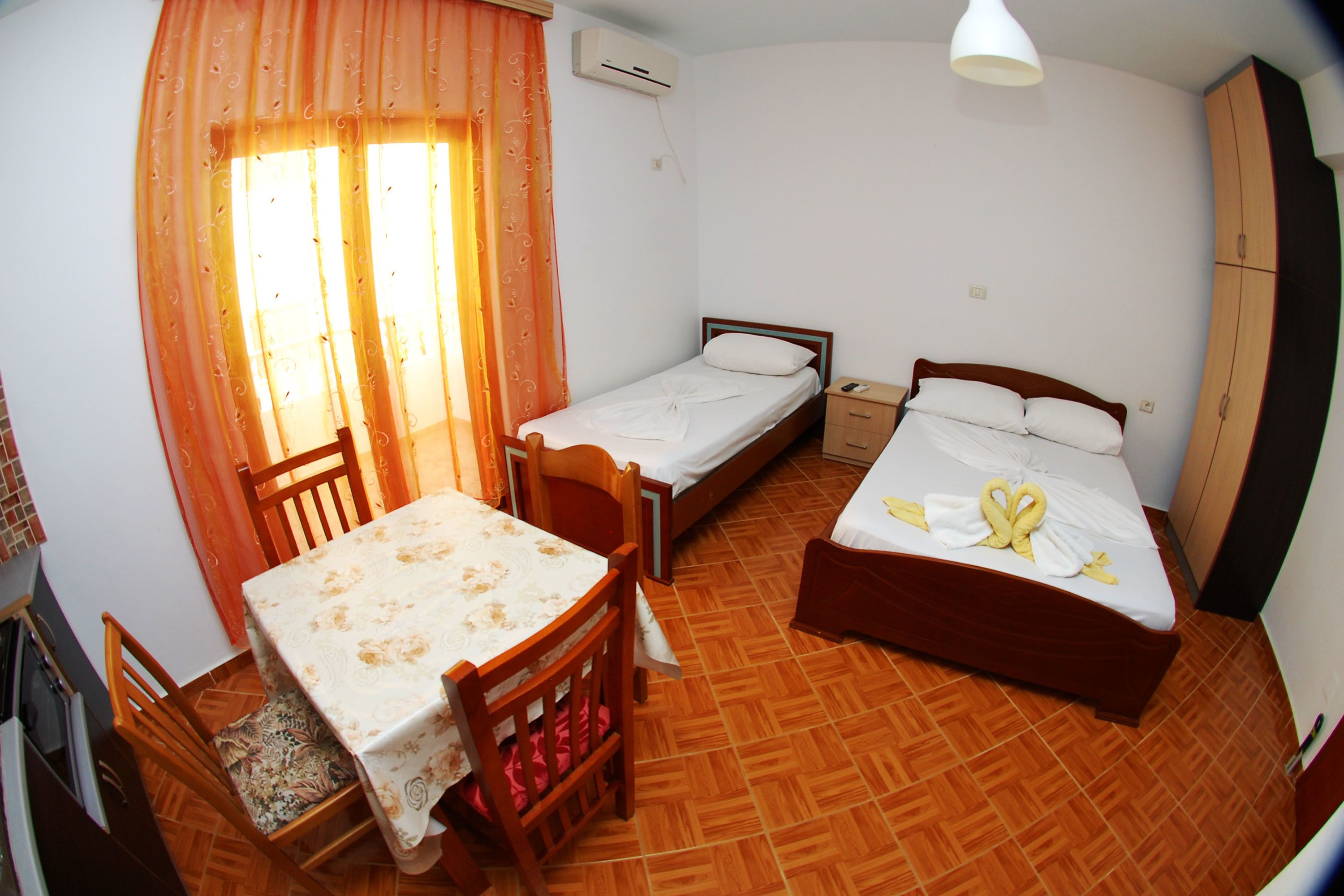 A room with two single beds, a wooden table with chairs, a small desk, and a wardrobe.