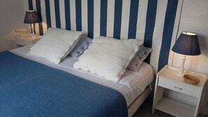 Una cama con ropa blanca y dos almohadas, flanqueada por dos mesitas de noche con lámparas y una pequeña cesta.