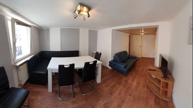 Un espacio habitable compacto con una mesa de comedor, sillas negras, un sofá y un televisor sobre un mueble de madera.
