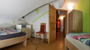 Un dormitorio con cama altillo, un escritorio y una silla. Hay un armario de madera y una puerta que da a otra habitación.