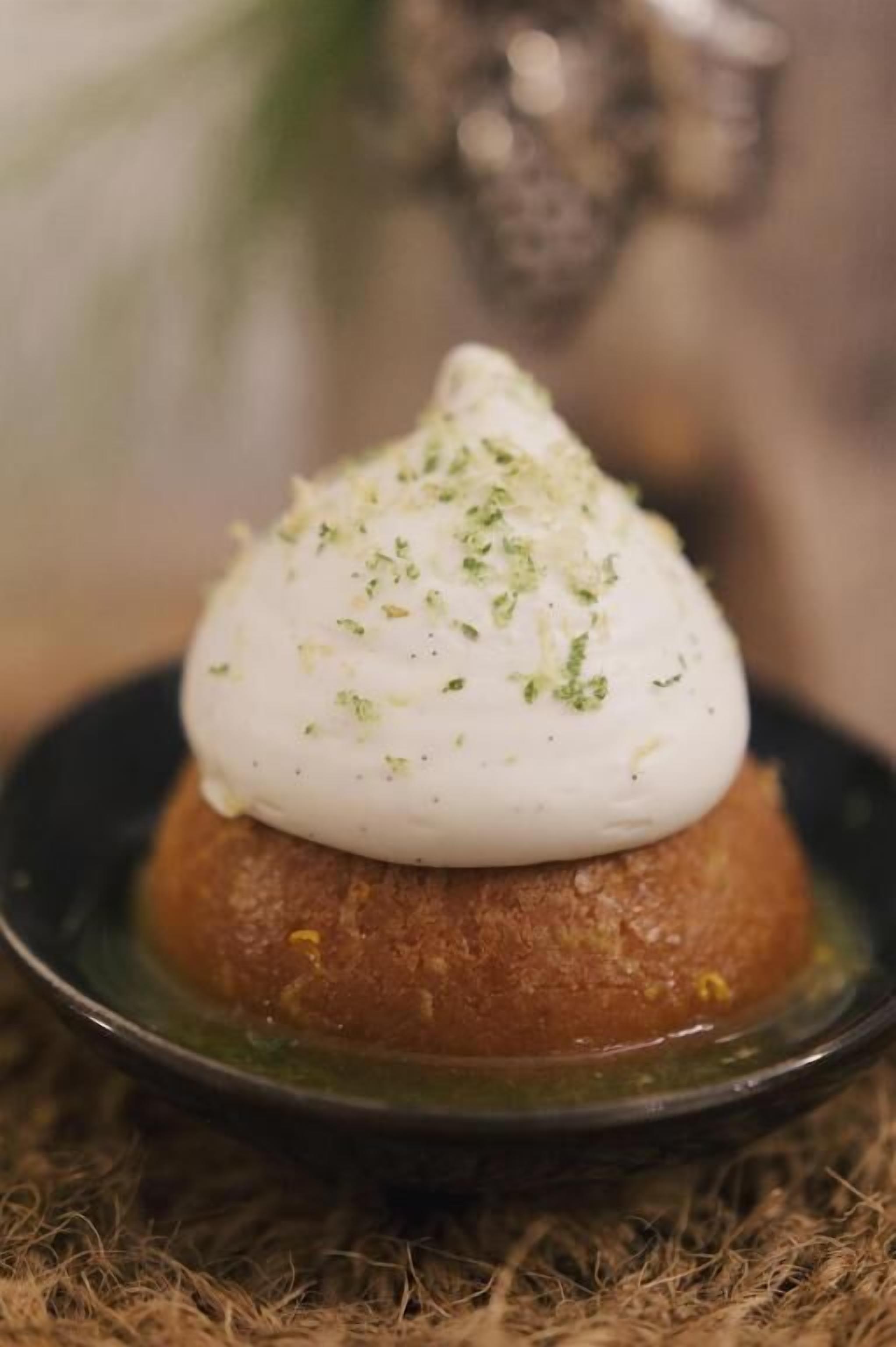 A dessert with a creamy topping on a round base, served on a dark plate.