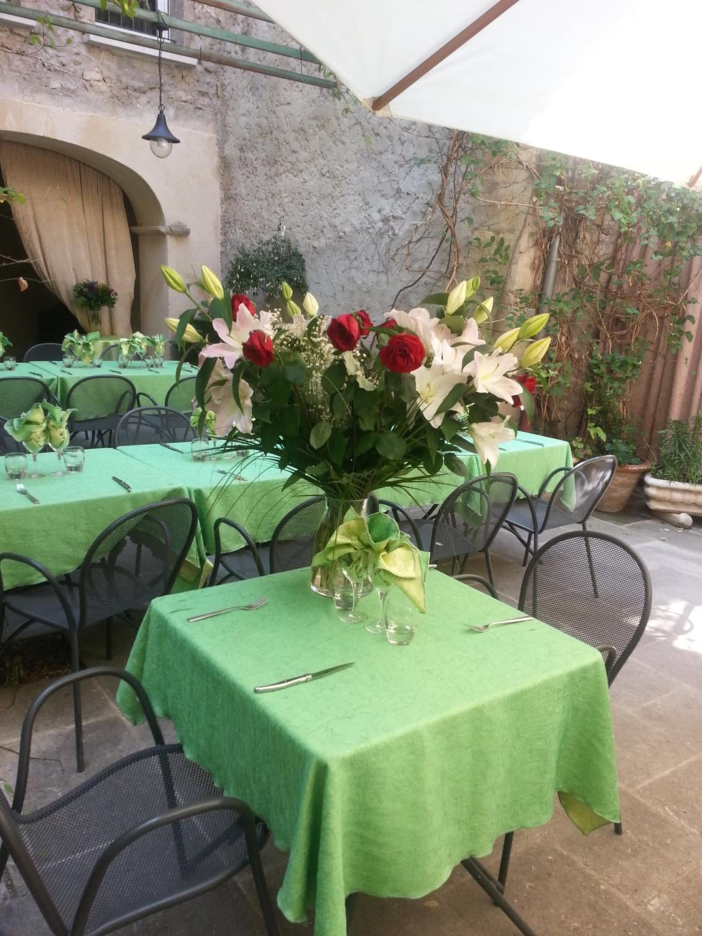 An outdoor dining area with tables covered in green tablecloths, chairs, and a central floral arrangement.