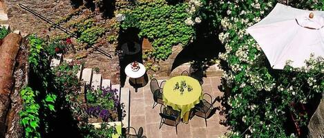 An outdoor patio with stone flooring, surrounded by lush greenery and flowering plants.