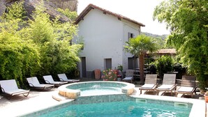 Une piscine avec des chaises longues, un jacuzzi et un bâtiment doté d’un toit en tuiles.