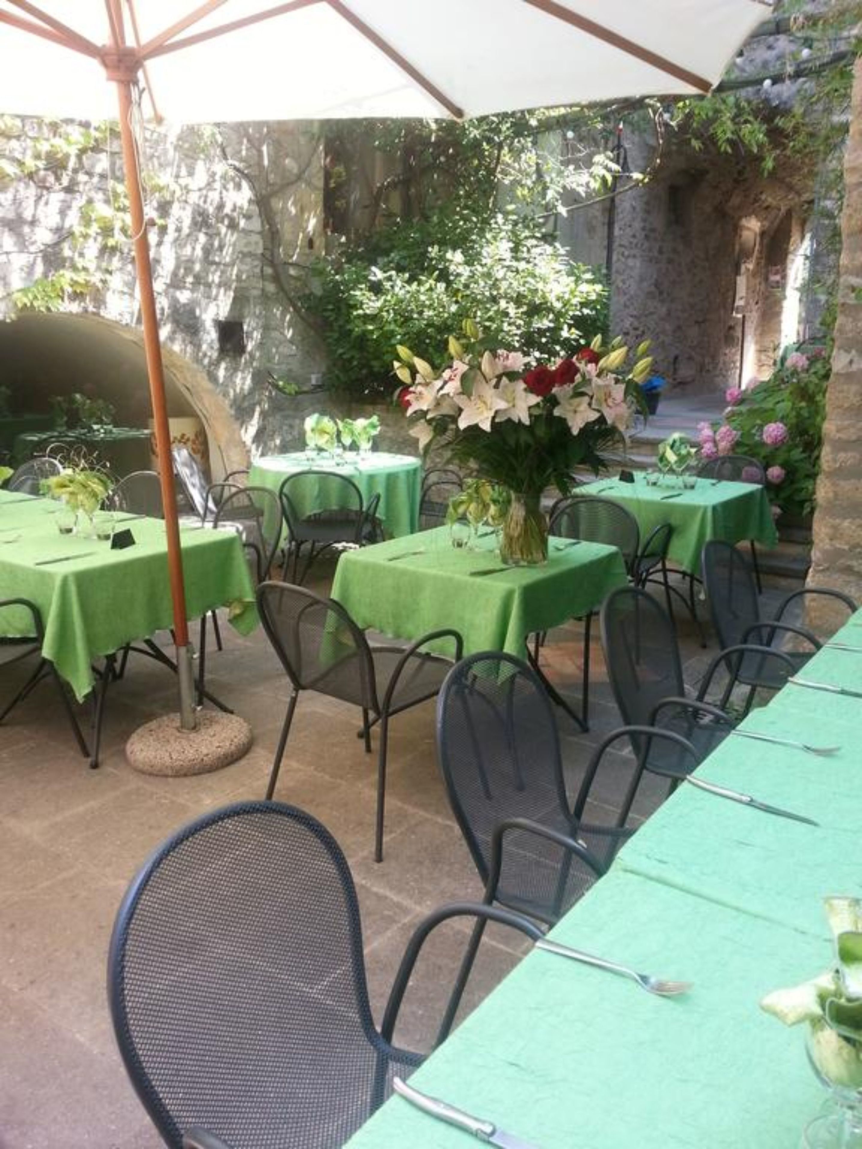 Ein Essbereich im Freien mit Tischen, die mit grünen Tischdecken bedeckt sind, Metallstühlen und einem großen Blumenarrangement.