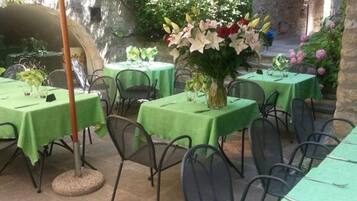 An outdoor dining area with tables covered in green tablecloths, metal chairs, and a large floral centerpiece.