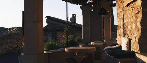 An outdoor patio with stone walls, a wooden ceiling, and tables with candles.