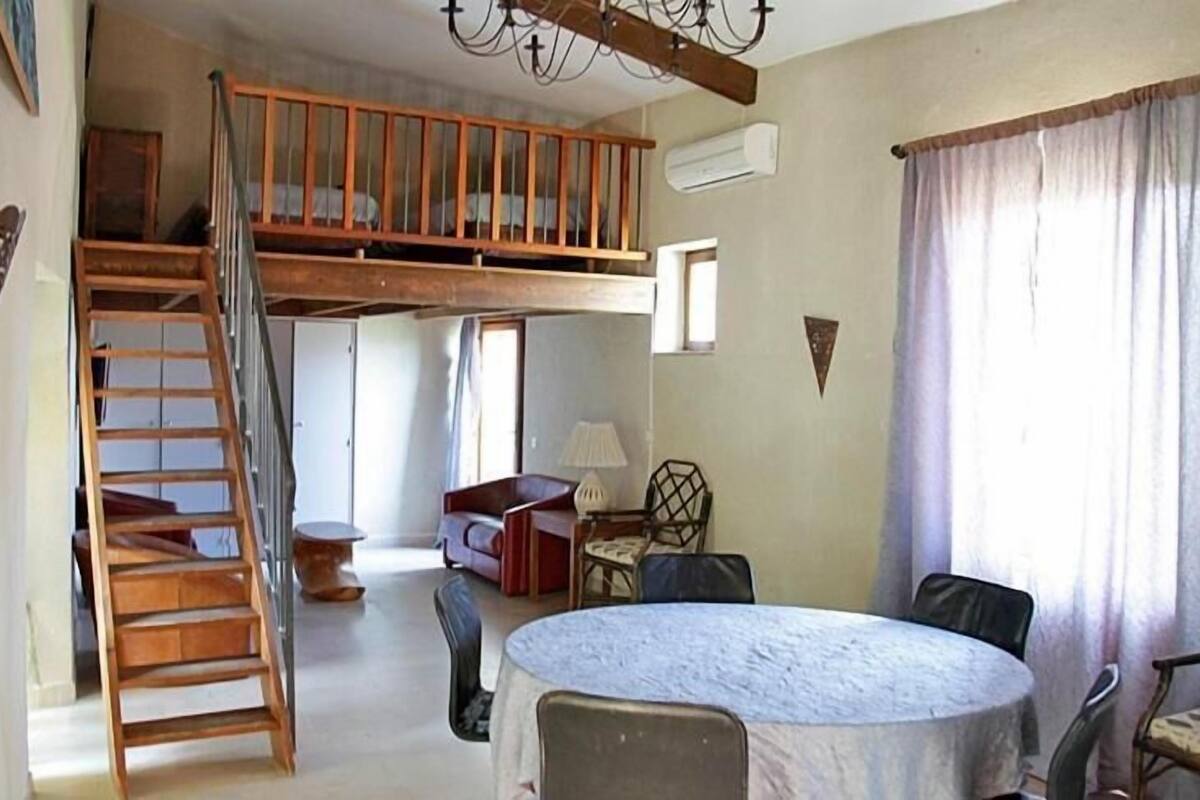 Une pièce avec un lit en mezzanine, une table de salle à manger ronde et un escalier.