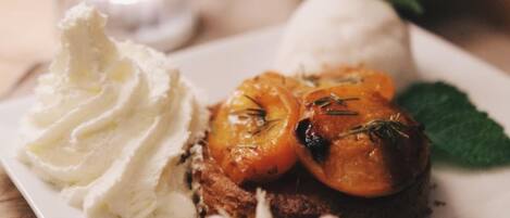 Un plato de postre con un pastel, fruta asada y crema batida.