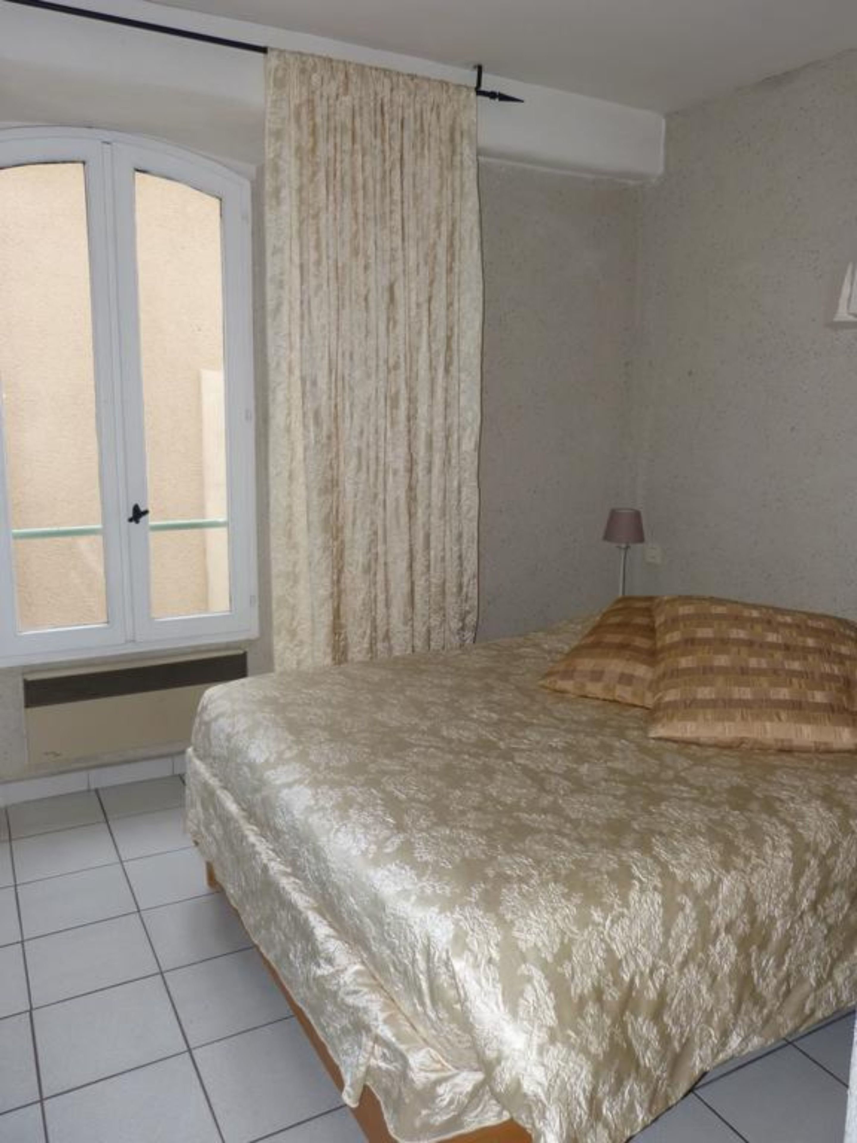 A bedroom with a bed, a window with curtains, and a lamp.