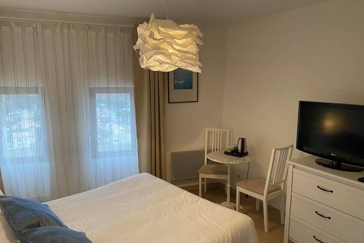 Une chambre d’hôtel avec un lit, une télévision, une petite table avec une chaise et une lampe en papier originale.