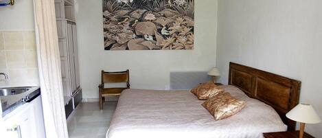 A bedroom with a bed, two pillows, a nightstand, a lamp, a chair, and a wall-mounted artwork.