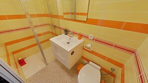 A bathroom with a white sink, toilet, and shower. The walls are tiled with a yellow and orange pattern.