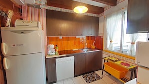 A compact kitchen with wooden cabinets, a white refrigerator, a coffee maker, and a small table with a colorful tablecloth.