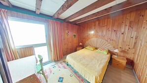 A bedroom with wooden walls, a bed with a yellow blanket, a fan, and a nightstand.