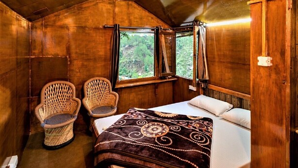 Une chambre confortable dans un chalet, avec un lit, deux fauteuils en osier et une fenêtre avec des rideaux.