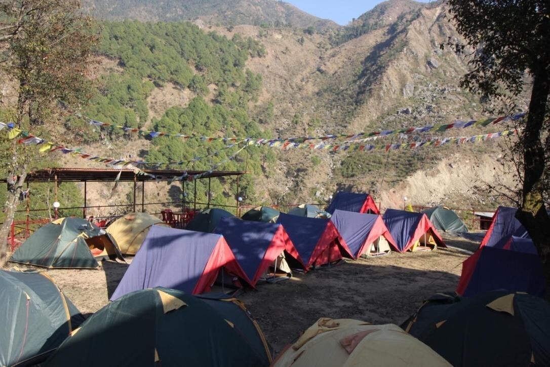 Un camping con varias tiendas de campaña dispuestas en filas, rodeado de terreno montañoso y un cielo despejado.