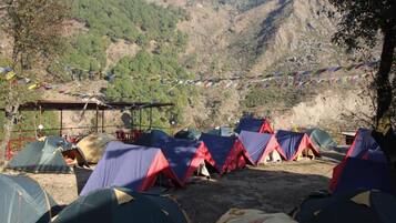 Un camping con varias tiendas de campaña dispuestas en filas, rodeado de terreno montañoso y un cielo despejado.