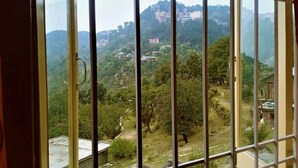 Une vue à travers une fenêtre grillagée sur une colline, avec des bâtiments et de la végétation.