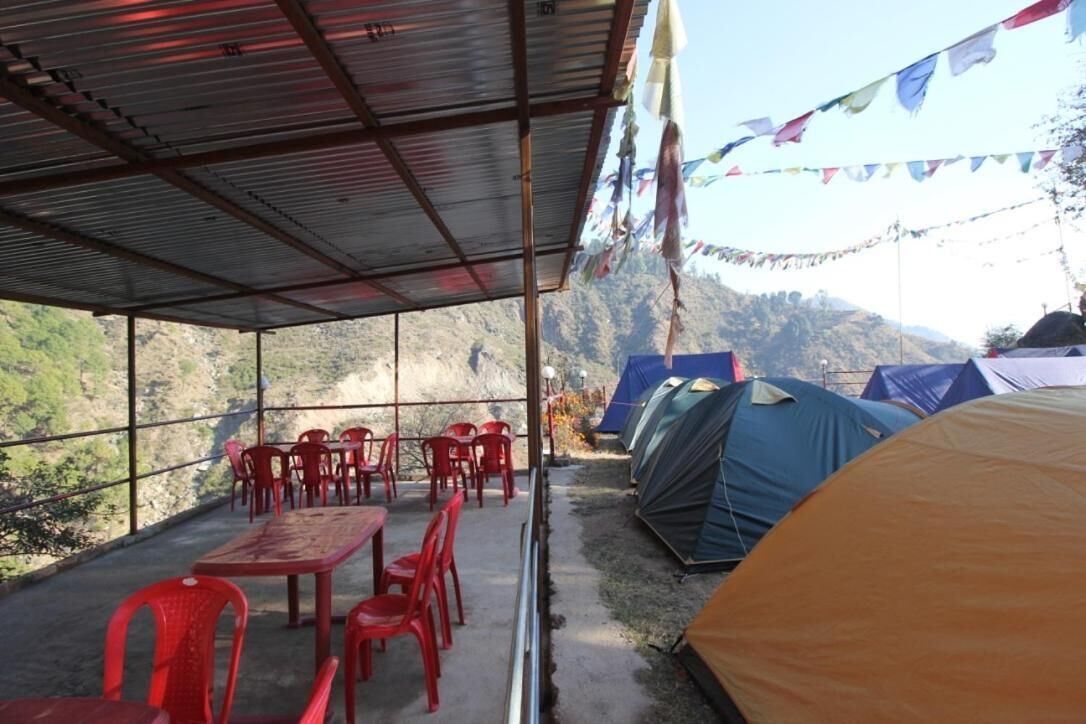 Un área de estar al aire libre cubierta con sillas y mesas de plástico rojo, rodeada de tiendas de campaña y un paisaje montañoso.