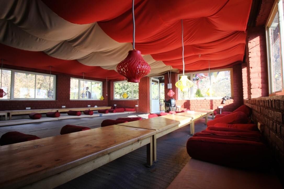 A room with long wooden tables and red cushions, large windows, and hanging red lanterns.