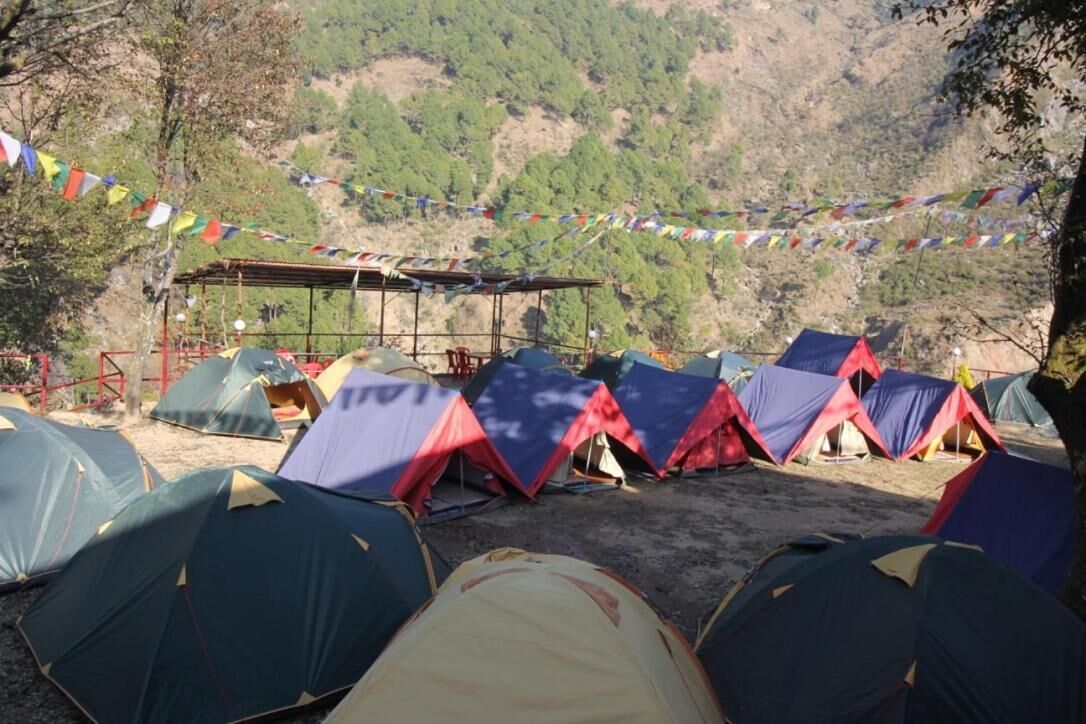 A campsite with multiple tents arranged in rows, a covered seating area, and colorful prayer flags strung between trees.
