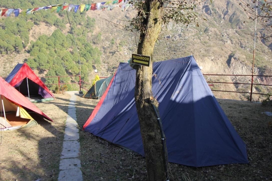 Um camping com tendas, um letreiro de banheiro e montanhas ao fundo.