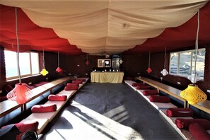 A room with long benches, red cushions, and hanging lamps. - Triund Camps Riverside Resort (Dharamshala)