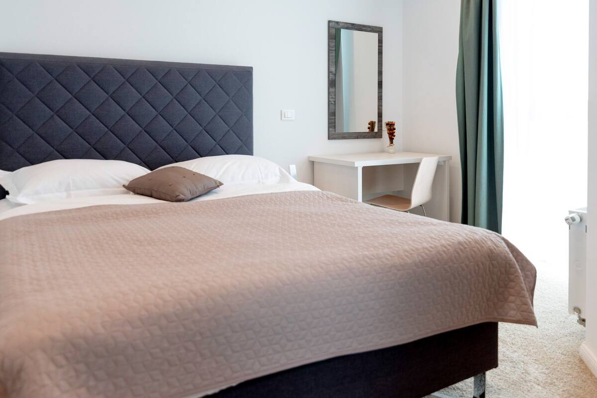 Un lit bien fait, avec une couverture matelassée, une tête de lit sombre et une table de chevet dotée d’un miroir.