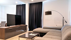 Een moderne woonkamer met een flatscreen televisie op een houten kast, een bank, een salontafel en een vloerlamp.