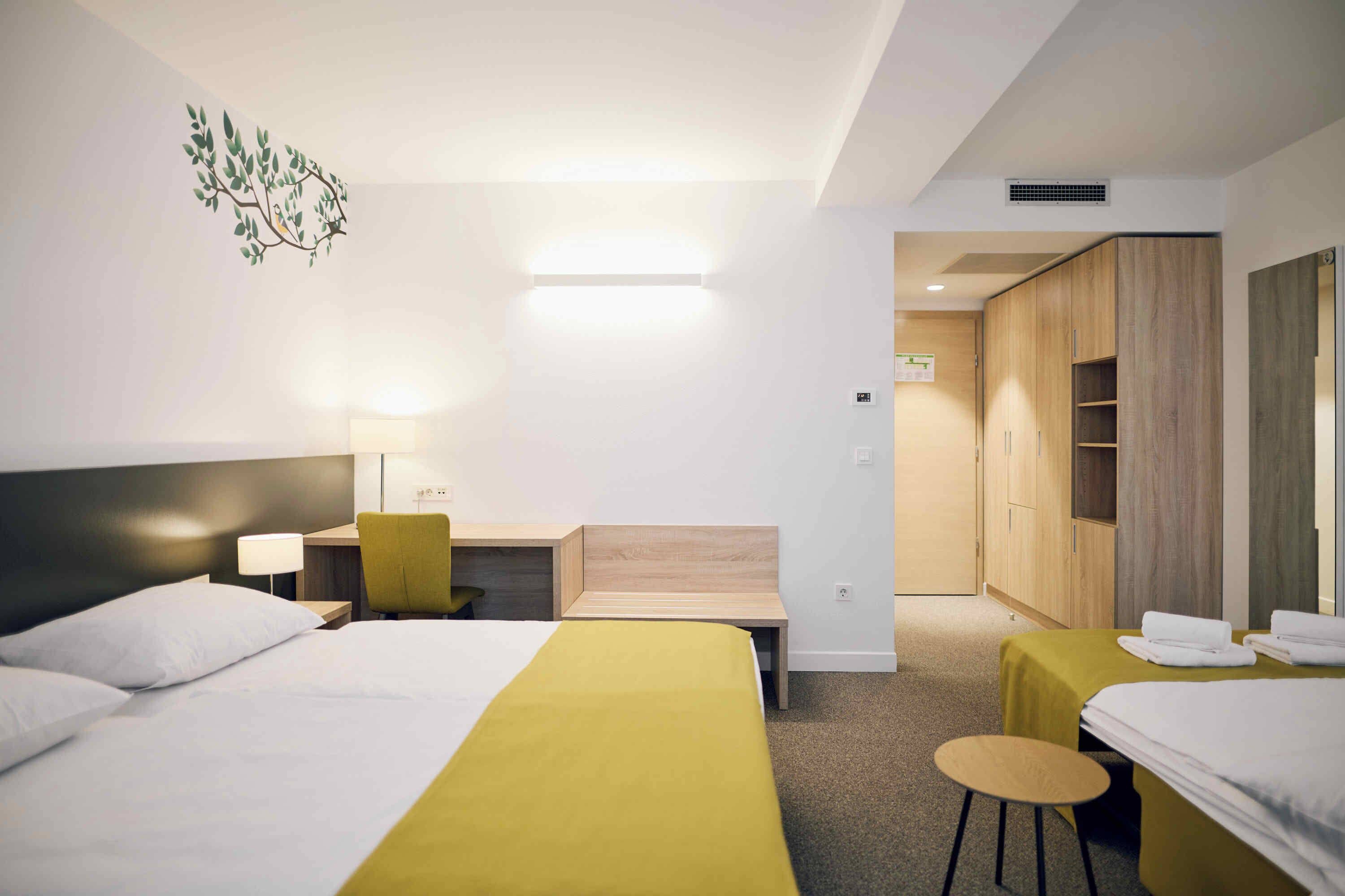 Habitación de hotel con dos camas, un escritorio, una silla y un armario.