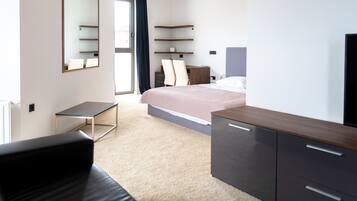 A modern hotel room with a bed, a desk, a chair, a TV, and a wardrobe.