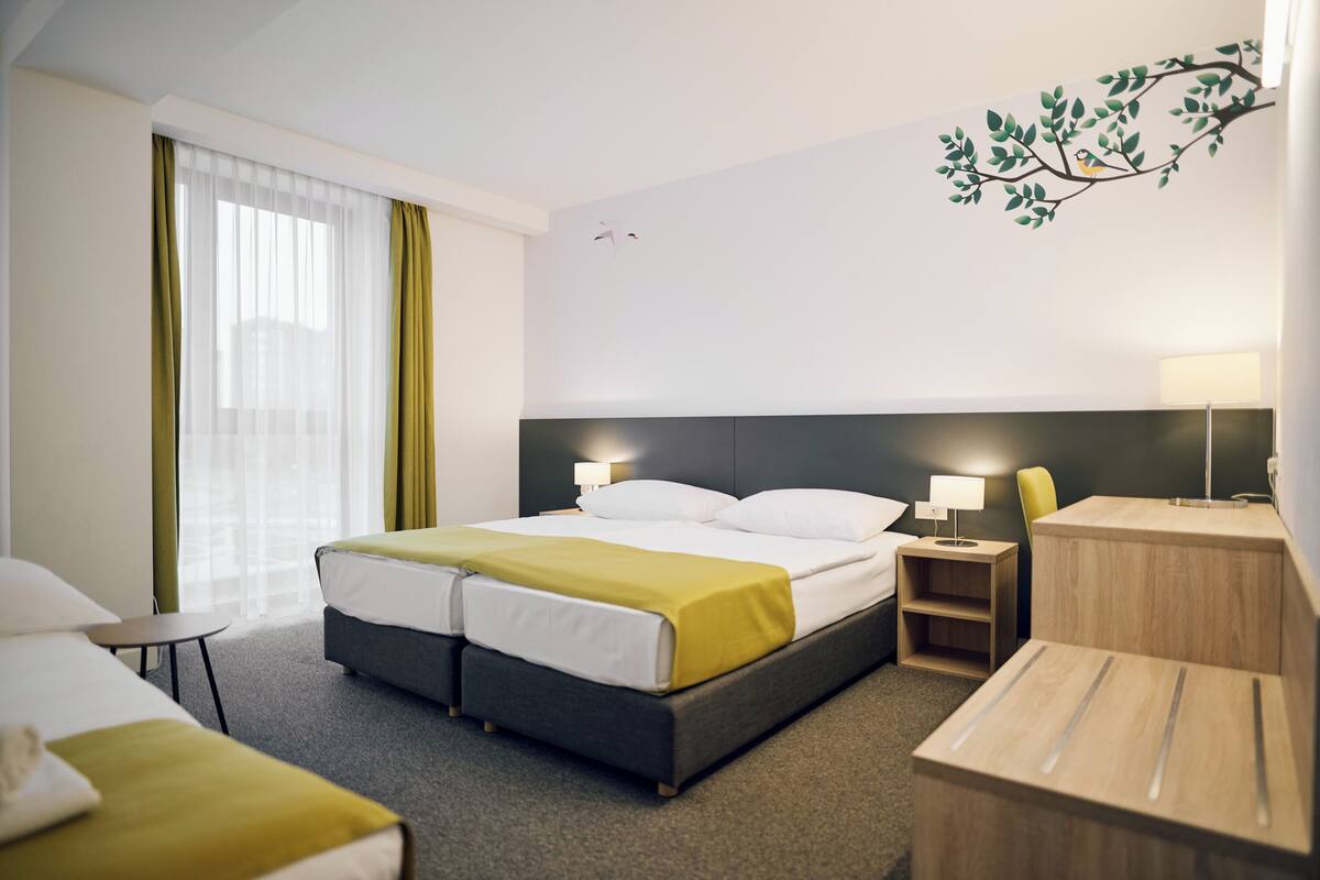 Une chambre d’hôtel moderne avec un grand lit, deux tables de chevet, un petit bureau et une chaise.