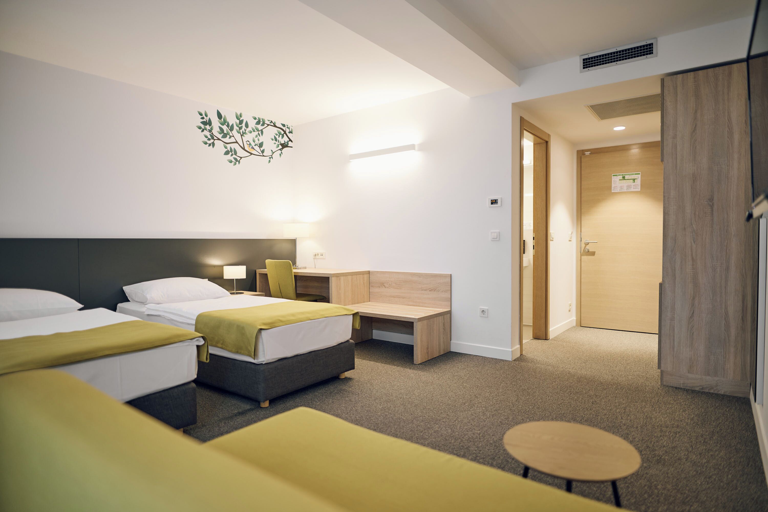 A hotel room with two beds, a desk, a chair, and a small table.