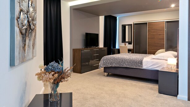 Een moderne slaapkamer met een bed, nachtkastje, kaptafel en een televisie.