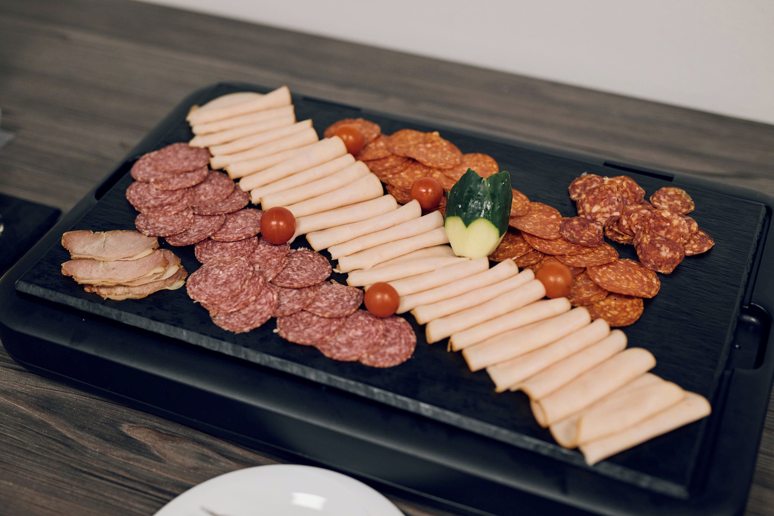 Un plateau noir contenant différentes sortes de viandes et de fromages, posé sur une table en bois.