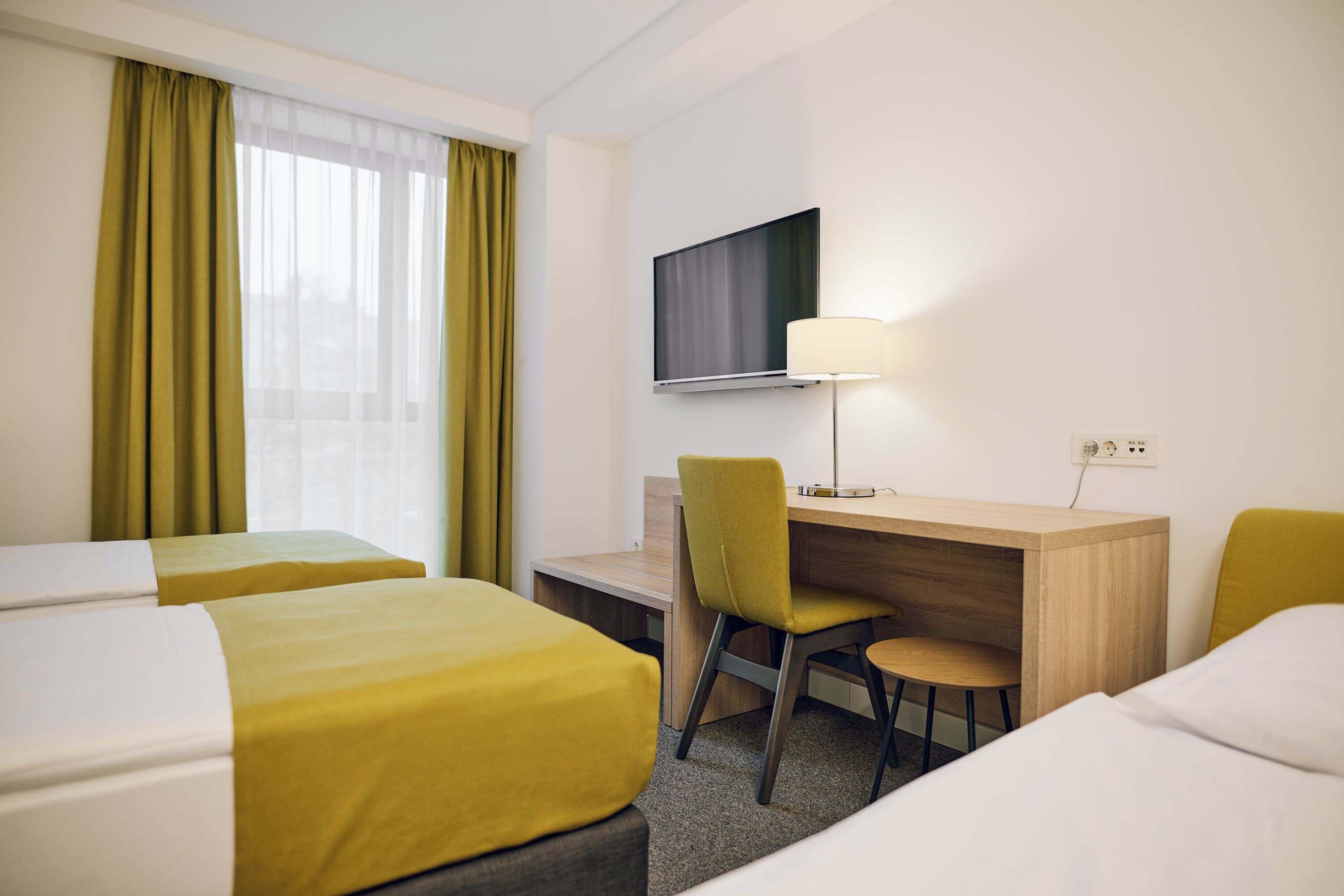 Ein Hotelzimmer mit zwei Betten, einem Schreibtisch, einem Sessel, einem Fernseher und einer Lampe.