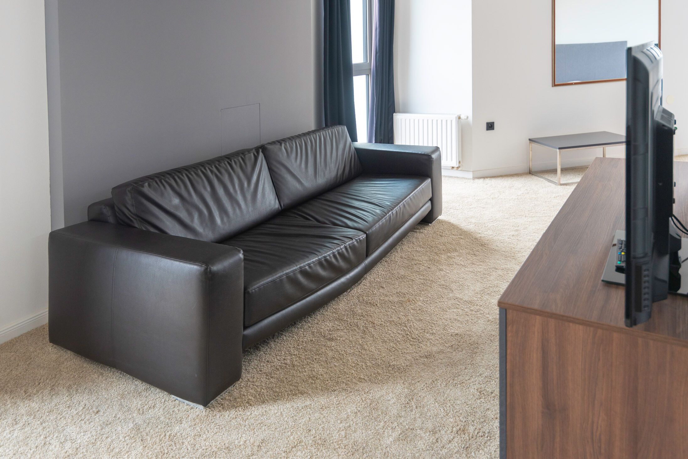 A modern living room with a black leather sofa, a wooden coffee table, and a television on a wooden stand.