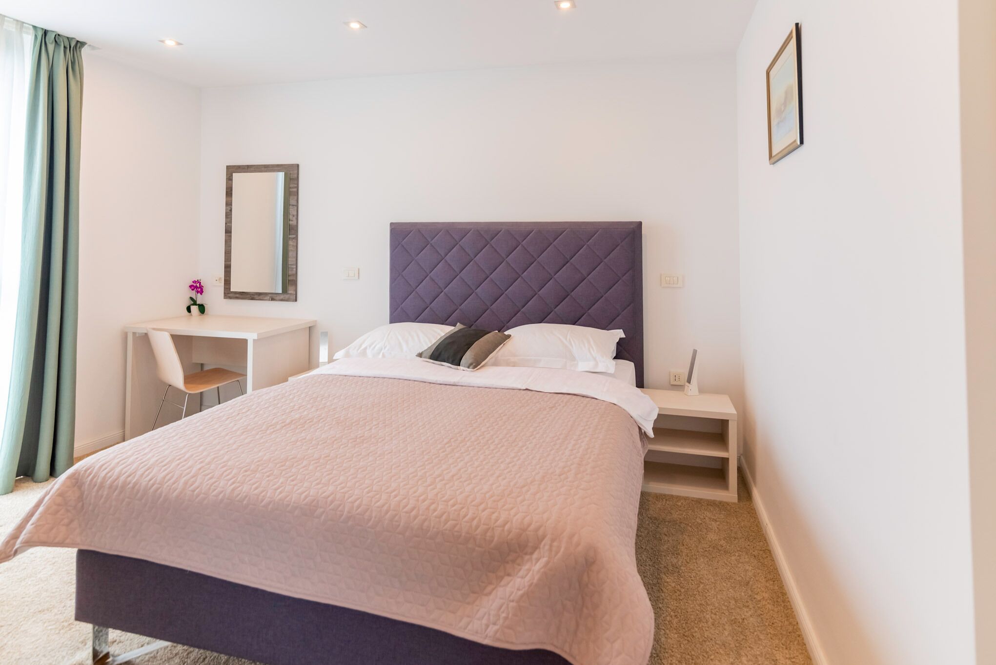 A bedroom with a bed, bedside tables, a mirror, and a desk.