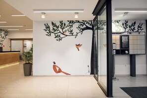 Un espace d’accueil moderne agrémenté d’une fresque représentant des oiseaux dans un arbre, d’un comptoir d’accueil en bois et d’une plante en pot.
