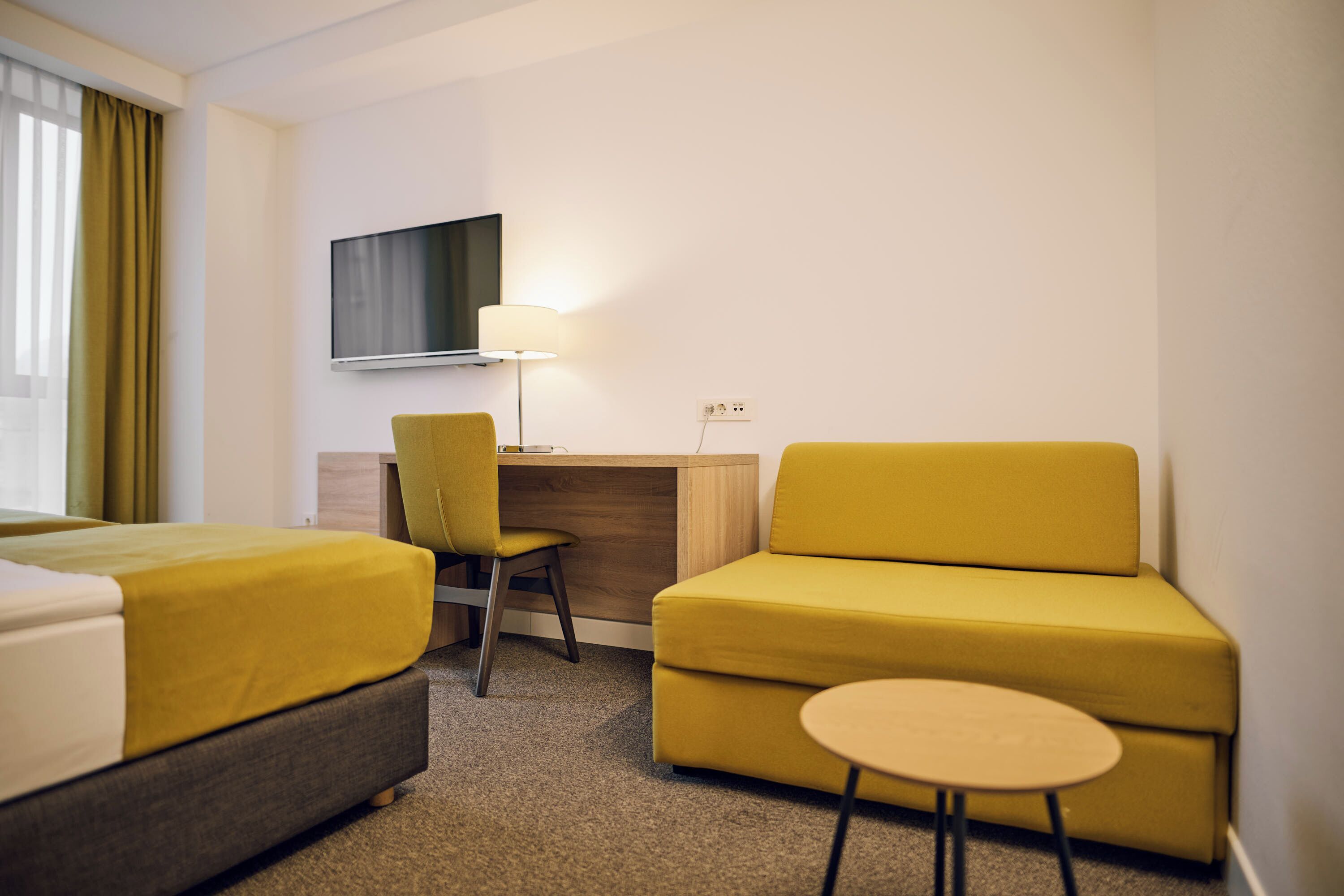 A hotel room with two beds, a desk, a chair, a sofa, and a small table.