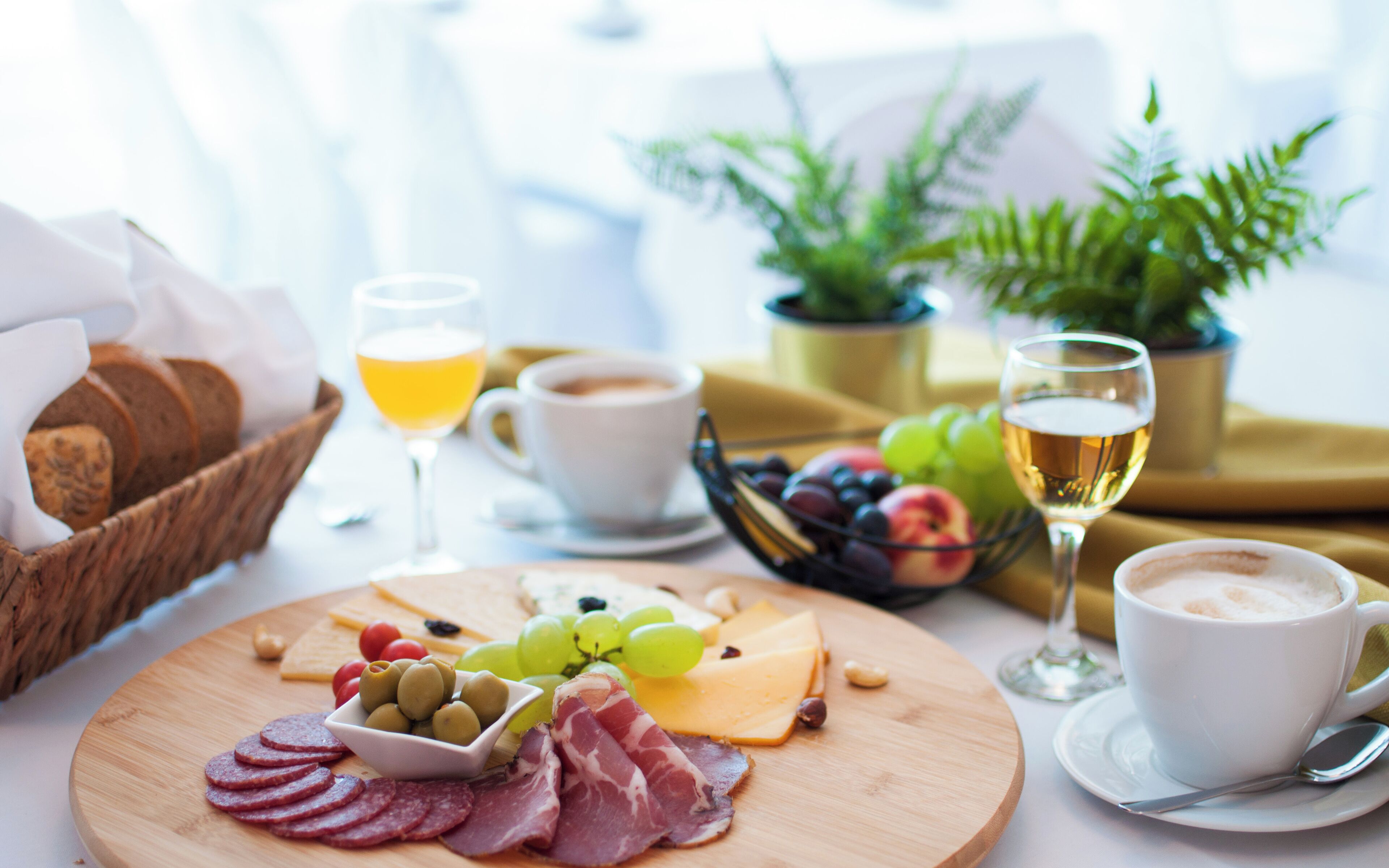 Une table en bois dressée pour le petit-déjeuner, avec une variété d’aliments et de boissons, notamment du fromage, de la charcuterie, des olives, des raisins et du café.