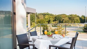 Een balkon met een ontbijttafel, rieten stoelen en uitzicht op een park en rivier.