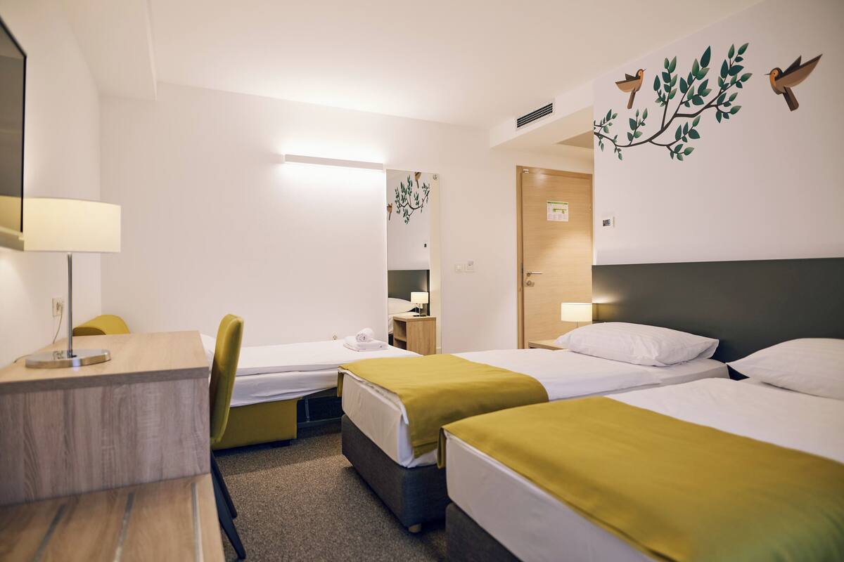 Une chambre d’hôtel avec deux lits simples, un bureau avec une lampe, une chaise et un miroir.