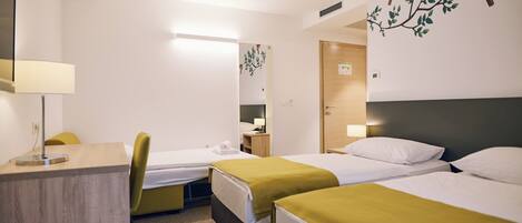 A hotel room with two single beds, a desk with a lamp, a chair, and a mirror.