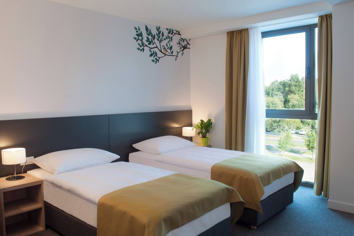 Une chambre d’hôtel avec deux lits, une table de chevet, une fenêtre avec des rideaux et un élément décoratif mural.