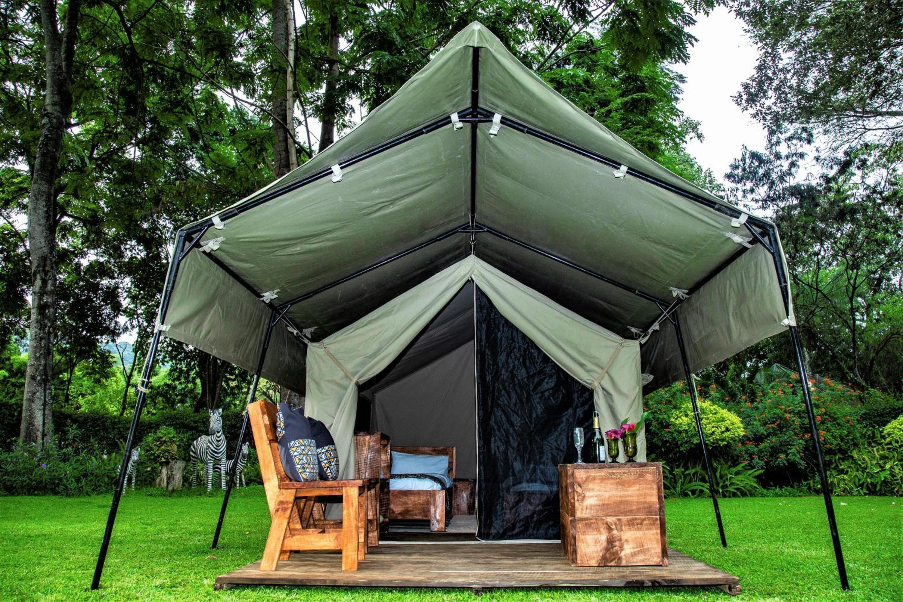 A tent with a wooden table and chairs outside, surrounded by greenery.